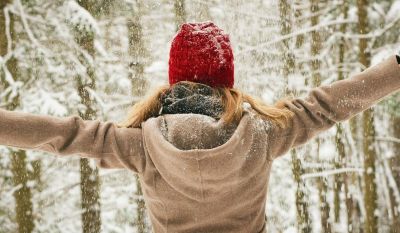 Freu im verschneiten Winterwald, die freudig die Arme ausbreitet