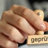 Hand die einen Stempel hält, auf dem geprüft steht
