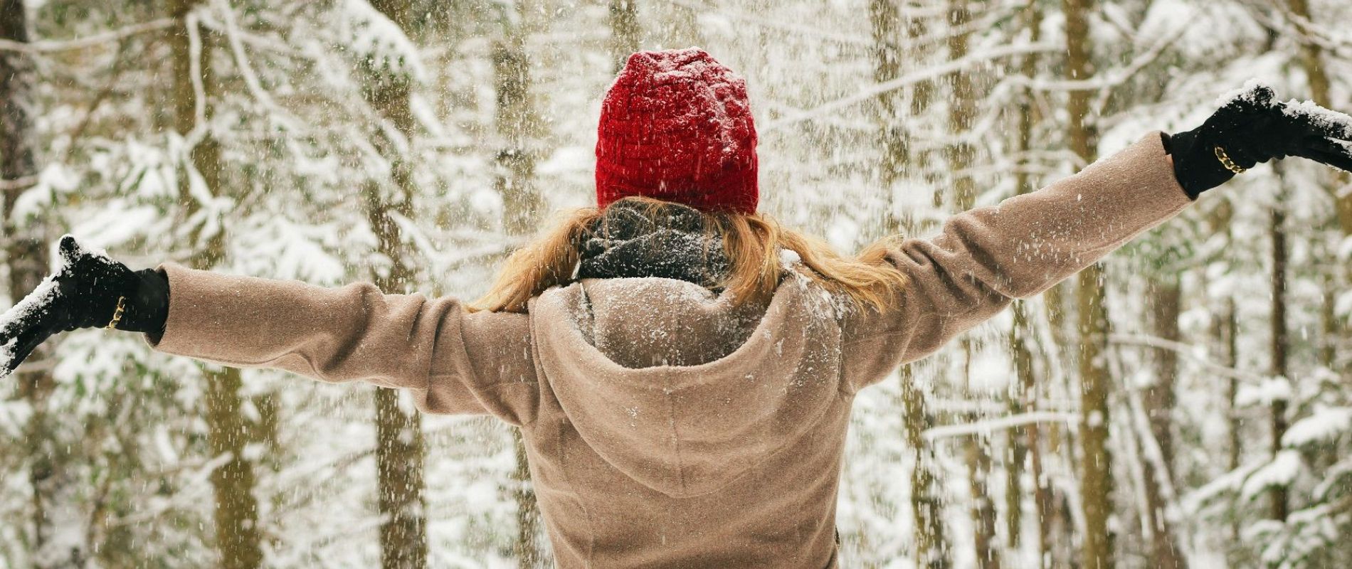 Freu im verschneiten Winterwald, die freudig die Arme ausbreitet