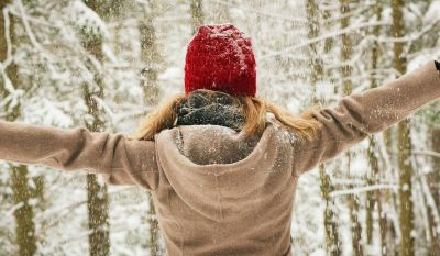 Freu im verschneiten Winterwald, die freudig die Arme ausbreitet