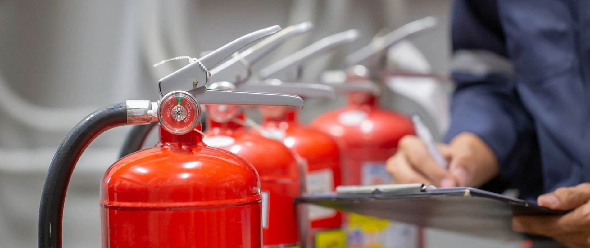 Feuerlöscher aufgereiht, man sieht eine Hand, die auf einem Klemmbrett etwas einträgt